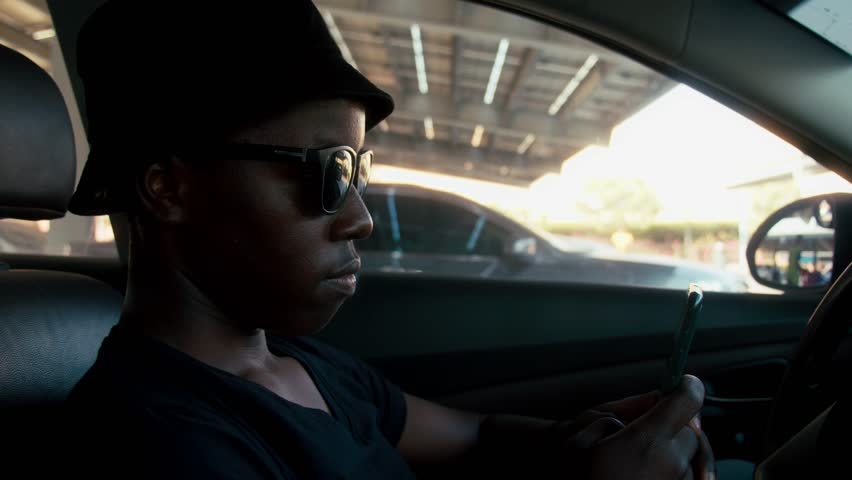 African american man typing a message on the phone while sitting in the car.
