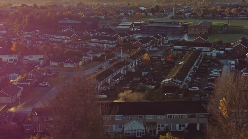 UK Townhouse estate suburb aerial view with early morning sunrise light leaks over Autumn coloured trees and rooftops