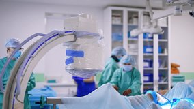 Spacious surgery room with modern equipment and a patient prepared for operation. C-Arm x-ray machine is near the operational table. Medical staff walks at backdrop. - Powered by Shutterstock - Get 15% off with code: PIKWIZARD15