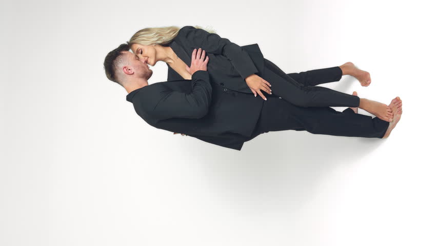 Beautiful Caucasian couple wearing similar black suits embracing and kissing in studio. Man and woman in love at white backdrop. Vertical screen. Royalty-Free Stock Footage #1111305473