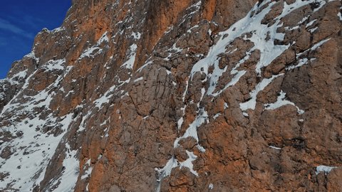 A drone view of a herd of mountain goats running the Steep slope.Wild mountain goats on rugged cliffs on a snowy day.They climb the steep cliff.Mountain goats living in mountainous.Great natural view. Stockvideó