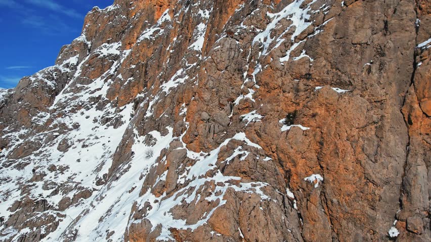 A drone view of a herd of mountain goats running the Steep slope.Wild mountain goats on rugged cliffs on a snowy day.They climb the steep cliff.Mountain goats living in mountainous.Great natural view. Royalty-Free Stock Footage #1111307193