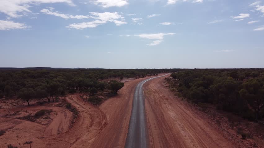 Drone ascending over a very remote country road surrounded with red soil and trees in the Australian outback