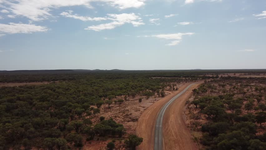 Drone flying over a very remote country road surrounded with red soil and trees in the Australian outback