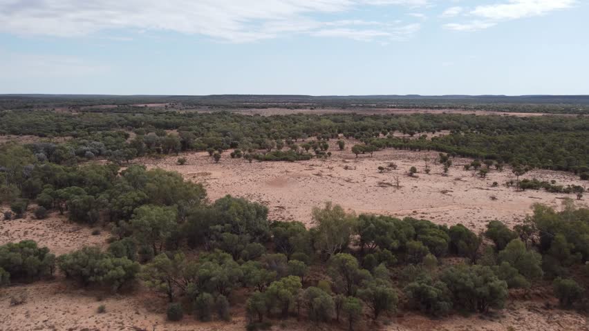 Drone flying over a remote Australian outback land with trees and some bold patches