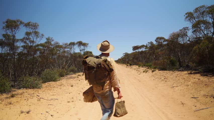 A historical looking swagman stand on a remote outback road in Australia.