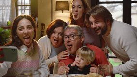A family sitting at a dining table chatting and laughing decides to take a family selfie.
During the photo, the whole family makes funny faces - Powered by Shutterstock - Get 15% off with code: PIKWIZARD15