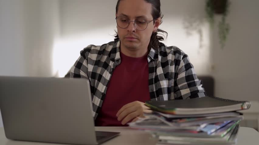 Stressed Young Man Amidst a Stack of Books and Laptop. Workload Overwhelm concept. Overworked and Struggling Royalty-Free Stock Footage #1111314905