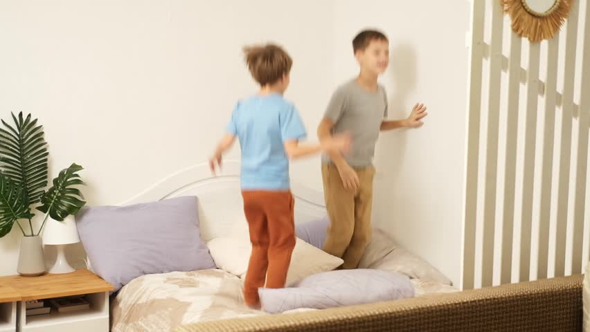 Portrait of children jumping on a bed, two boys have fun and laughing, happy kids at home.