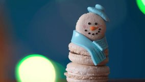 Snowman dessert macaron decorated with hat and scarf against colorful lights and bokeh background. Camera moves away from object. Merry Christmas and Happy New Year festive concept - Powered by Shutterstock - Get 15% off with code: PIKWIZARD15