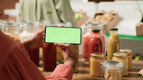 Young woman shops with greenscreen display on smartphone, choosing organic products sold in bulk from local grocery store. Vegan customer searching for locally grown eco friendly produce. - Powered by Shutterstock - Get 15% off with code: PIKWIZARD15