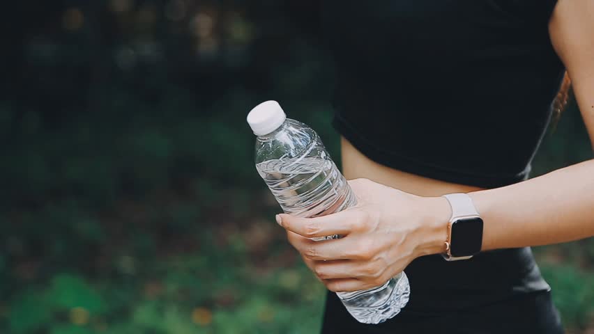 Energetic Break, Woman Athlete Refreshes During Hot Day Run, Highlighting a young woman athlete taking a break, drinking water, and staying hydrated during a run on a hot day. The scene promotes Royalty-Free Stock Footage #1111332125