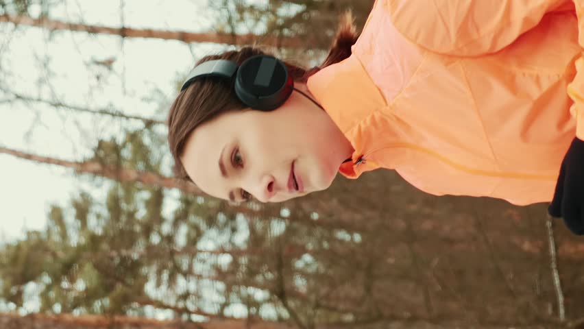 Female running in park. Young beautiful woman jogging in winter forest. Professional athlete runner in orange jacket running in snowy forest. Trail running. Intense cardio training. Vertical video