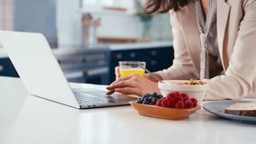 Businesswoman at home multi-tasking in kitchen working on laptop whilst eating breakfast and drinking orange juice - shot in slow motion - Powered by Shutterstock - Get 15% off with code: PIKWIZARD15