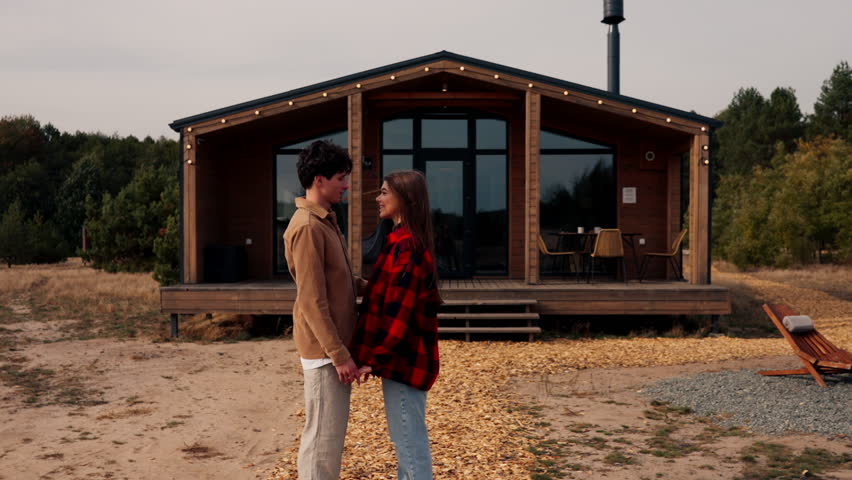 A girl and a guy in love looking into each others eyes holding hands and hugging standing outside house on the street