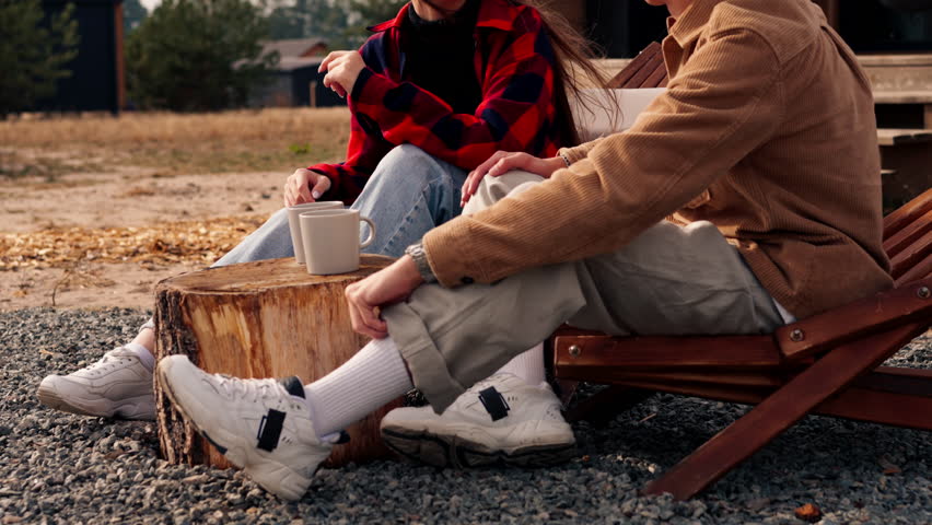 On the terrace near a large house a loving couple sits with cups of tea on wooden chairs and communicates with each other
