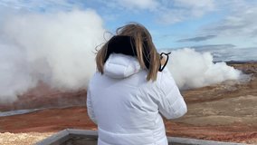Blonde tourist woman taking pictures with a reflex of a fumarole in Gunnuhver, Iceland.