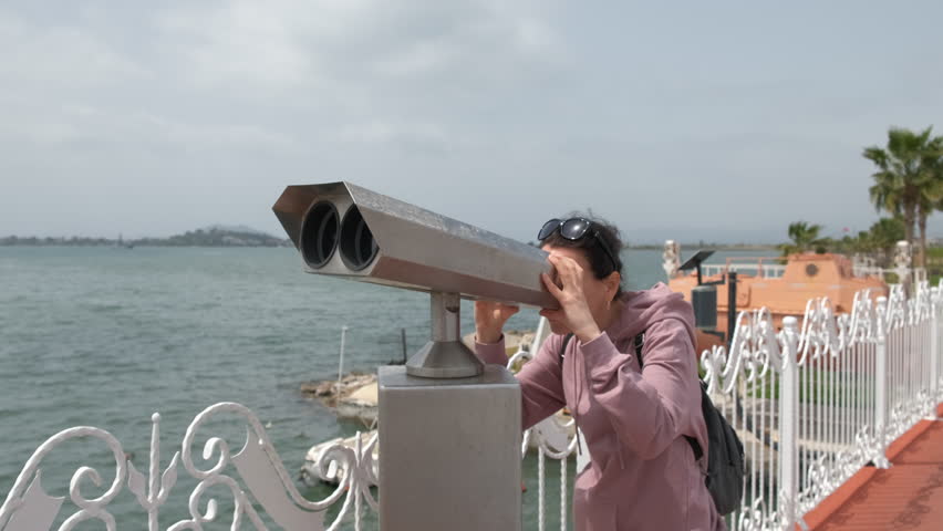 A woman looks through binoculars. Beautiful woman tourist on the seashore looks through binoculars.