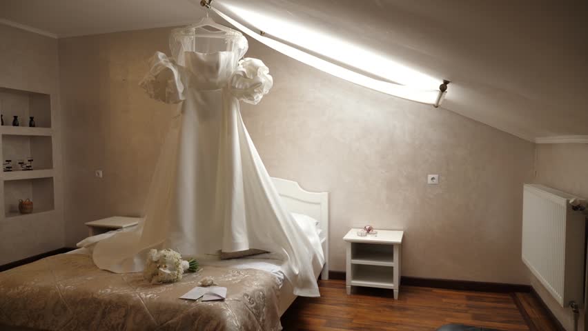 A beautiful white wedding dress hangs in the room. Preparation for the wedding ceremony.