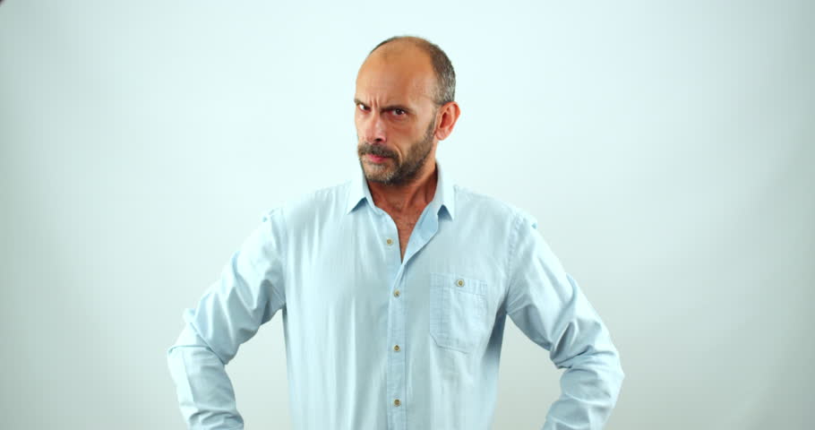 In the studio, a middle-aged man looks at the camera in slow motion and makes gestures and facial expressions that show that he is crazy with anger. Royalty-Free Stock Footage #1111347913