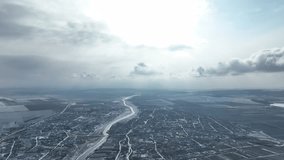 Aerial 4K video from a drone flying over the village and field, covered with snow. Winter season, cloudy sky 