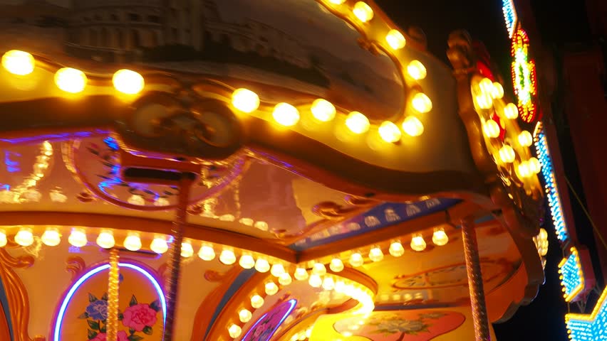 A carousel or carrousel, merry-go-round, roundabout, or hurdy-gurdy is amusement ride consisting of a rotating circular platform with seats for riders. Colorful flashing light of vintage carnival Royalty-Free Stock Footage #1111360417