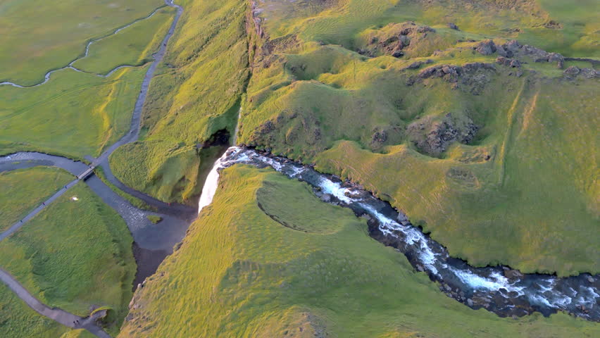 Breathtaking aerial footage of rock formations with vast territory of meadows blanketed with green grass and narrow cascade of the waterfall creating mist. High quality 4k footage Royalty-Free Stock Footage #1111362371
