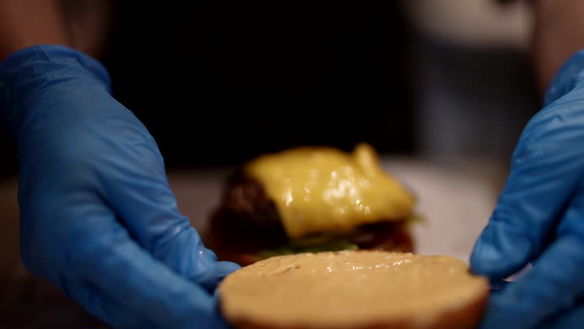 Cook assembling and packing hot tasty burger with beef cutlet and cheese, closeup view, fast food | Shutterstock HD Video #1111365495