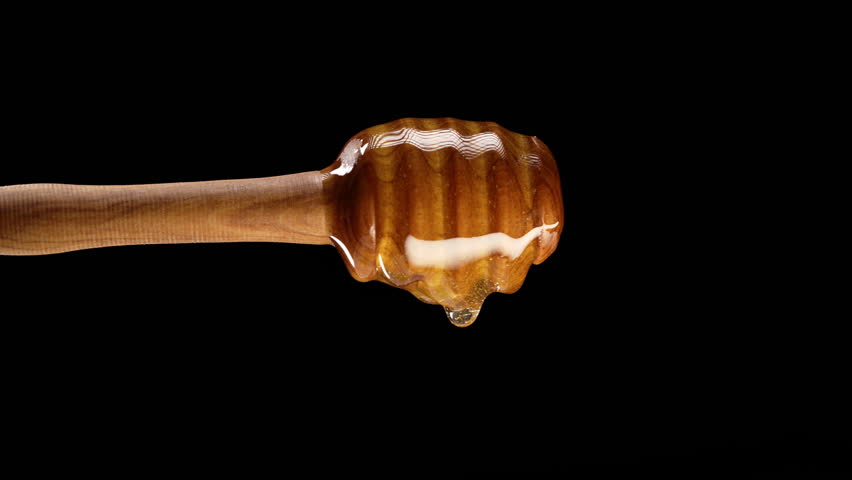 Natural wooden honey spoon: dipper stick with dripping honey on black background