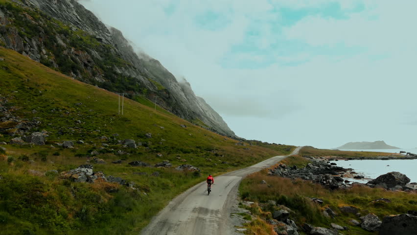 Camera follows cyclist riding bike in incredible epic landscape surrounded by mountains and fjord. Gravel cycling on dirt unpaved road in natural park Royalty-Free Stock Footage #1111370373