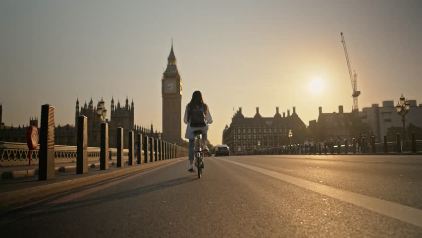 Tracking shot young tourist woman riding bicycle on Westminster Bridge London towards Big Ben at sunset. Concept of eco-friendly tourism transportation in London Royalty-Free Stock Footage #1111373275
