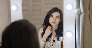 The girl looks in the mirror and applies makeup on her face. A woman eats at a make-up table and does cosmetic procedures. Apply the powder on the skin of the face with a brush.