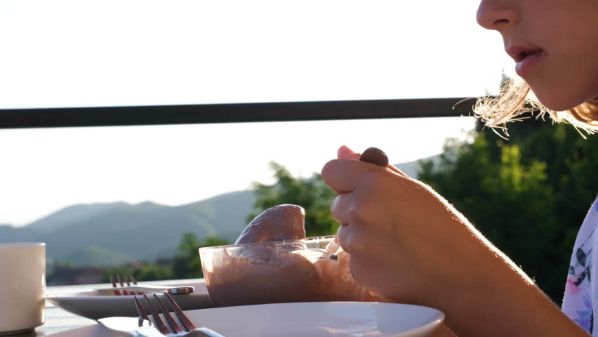 Cute little girl eating tasty ice cream while sitting on a terrace by the beautful view of nature at sunset