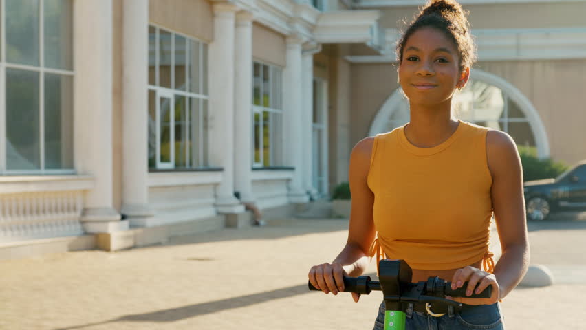 Portrait of beautiful mixed race woman with shared electric push scooter in the city. Rental electric transportation.