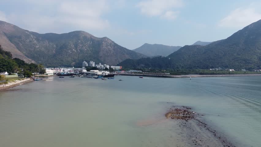 A drone view of a boat driving near the coast and green mountains on the horizon
