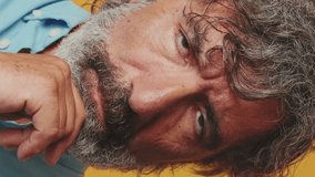 Vertical video, Close up portrait, elderly white-haired bearded man wears a blue shirt, shrugs her shoulders having no idea what to do next, isolated on an orange background in the studio - Powered by Shutterstock - Get 15% off with code: PIKWIZARD15