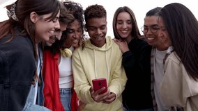 Happy diverse student friends laughing together while watching funny videos on smart phone. Young multiracial people having fun using social media mobile app