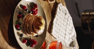 Sprinkling sugar powder on tasty pancake, slow motion. Close-up pancakes stack on plate decorated with berries and powdered sugar. Breakfast aesthetics, wooden table, morning sunlight. Vertical video