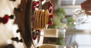 Unknown woman maple syrup drizzled perfectly arranged pancakes with raspberry over them, in slow motion. Cinematic vertical video. Yummy delicious gluten-free food options dessert cheat meal, recipes