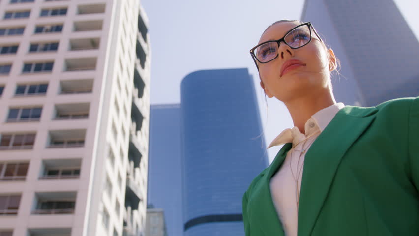Confident young woman in formal outfit looking around outside on street in financial district of modern urban city downtown. Businesswoman portrait low angle dolly.Beautiful modern manager slow motion