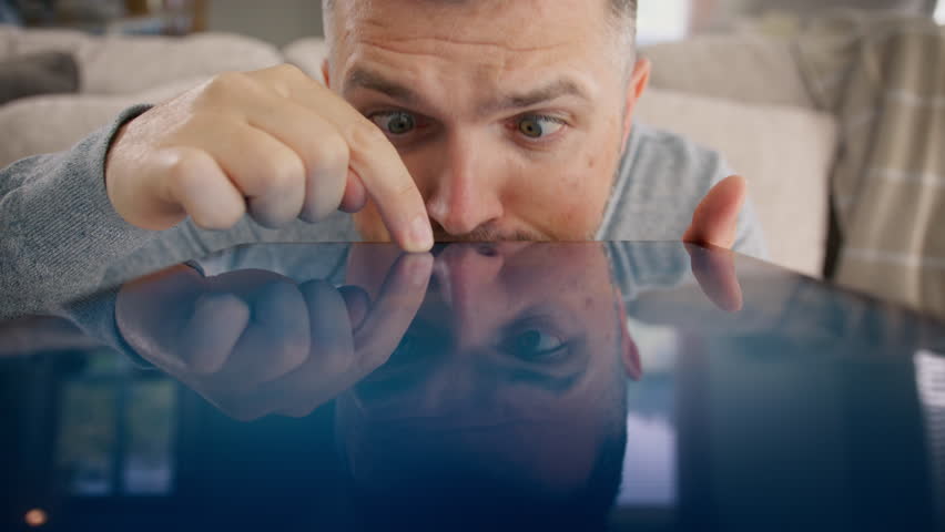 Hilarious man scrolls browsing internet using tablet. Comic man making silly funny faces. Humor Curious nerd search. Funny male eyes look closely on tablet devise screen trying find information online