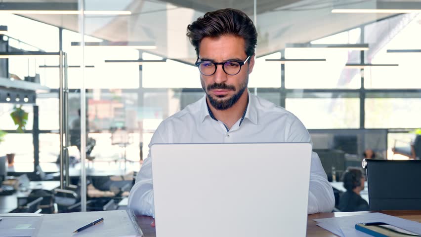 Busy young Latin business man looking at laptop at work. Focused young businessman company executive manager investor using computer sitting in office thinking of investment plan checking digital data Royalty-Free Stock Footage #1111405427