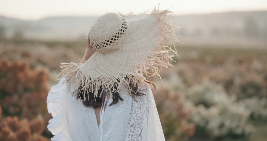 Woman with straw hat running across a field with large blooming flowers.