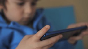 Closeup Child Playing Games In Phone at Home on Couch. Boy Playing Video Game on Mobile Phone. Preschooler Plays Video Game Smartphone on Sofa. Kid Using Phone for Gaming Online Education Social Media
