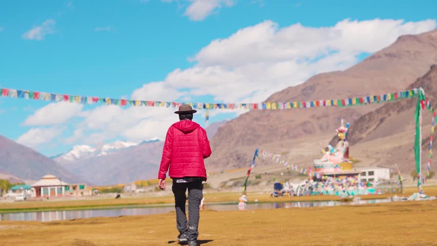 Rear View shot of an Indian tourist wearing hat walking in front of statue of Guru Padmasambhava besides the Sani lake in Sani village near Padum in Zanskar Valley, Ladakh, India. Tourist in Zanskar.
