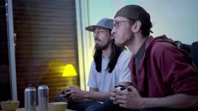 Two young Latin men college students playing with a video game console cheating and drink beer at night