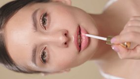 Beauty brunette woman applying lip gloss isolated on beige background. Vertical video. Makeup cosmetics - Powered by Shutterstock - Get 15% off with code: PIKWIZARD15