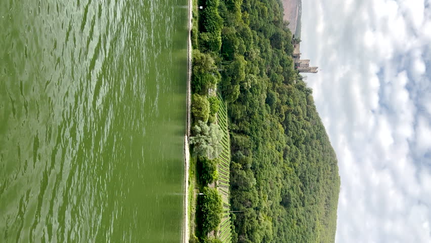 Traveling along the Rhine River with scenic views of the quaint village of Niederheimbach, Germany. Views of mountains and rolling hills with agricultural fields. 
