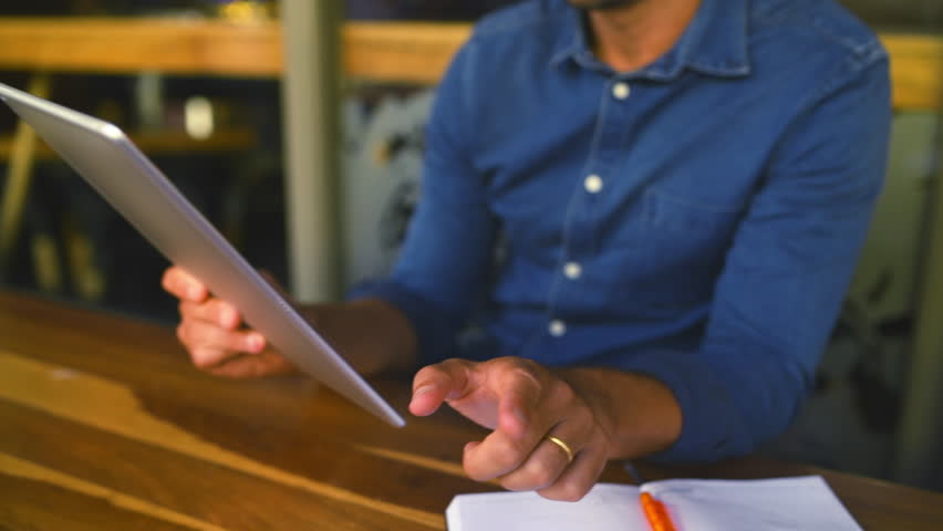 Hands, tablet and remote work in a coffee shop with a man entrepreneur at a table for research or planning. Technology, notebook and freelance business with an employee in a cafe or restaurant