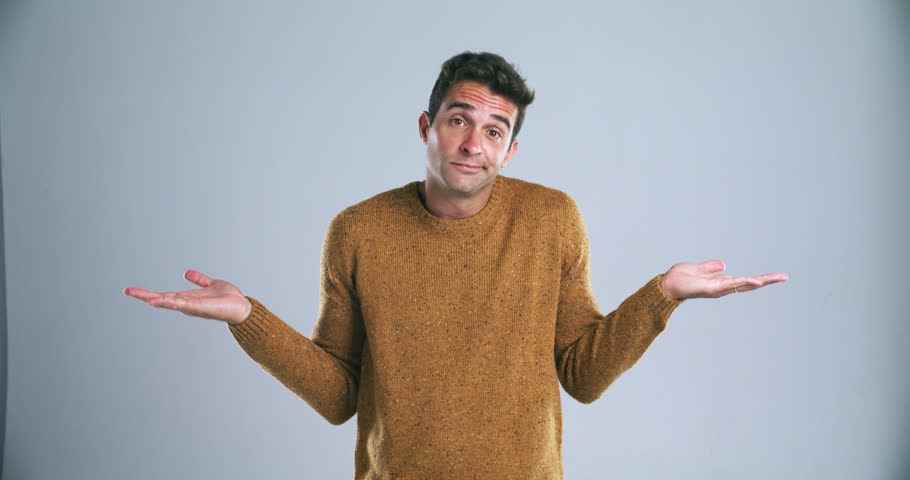 Confused, shrug and face of man in studio with decision, choice and dont know reaction. Thinking, wondering and portrait of person with hand gesture for unsure, doubt and what on blue background